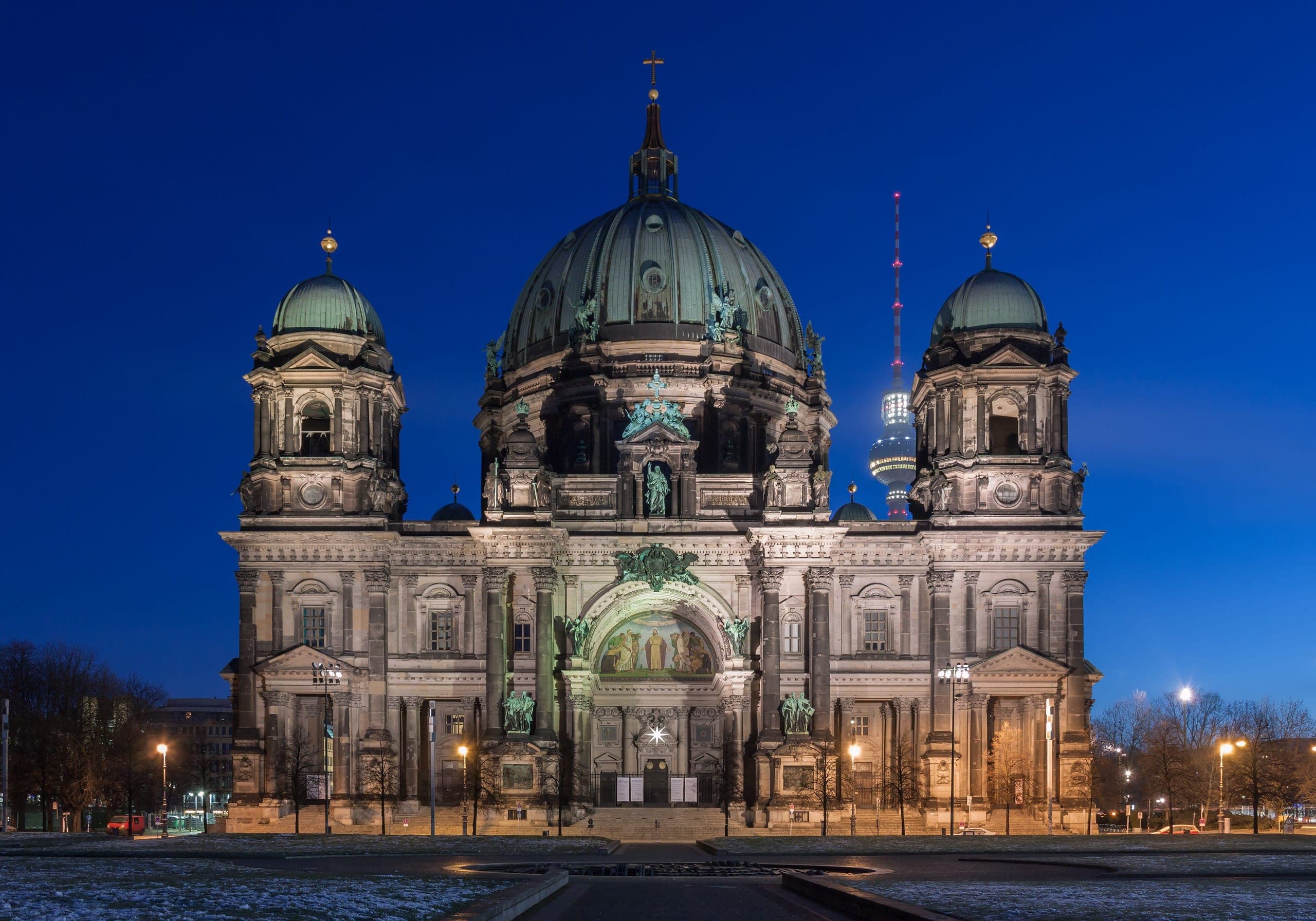 The Berliner Dom at night, its dome and stonework floodlit against a black sky, seen from across the water.