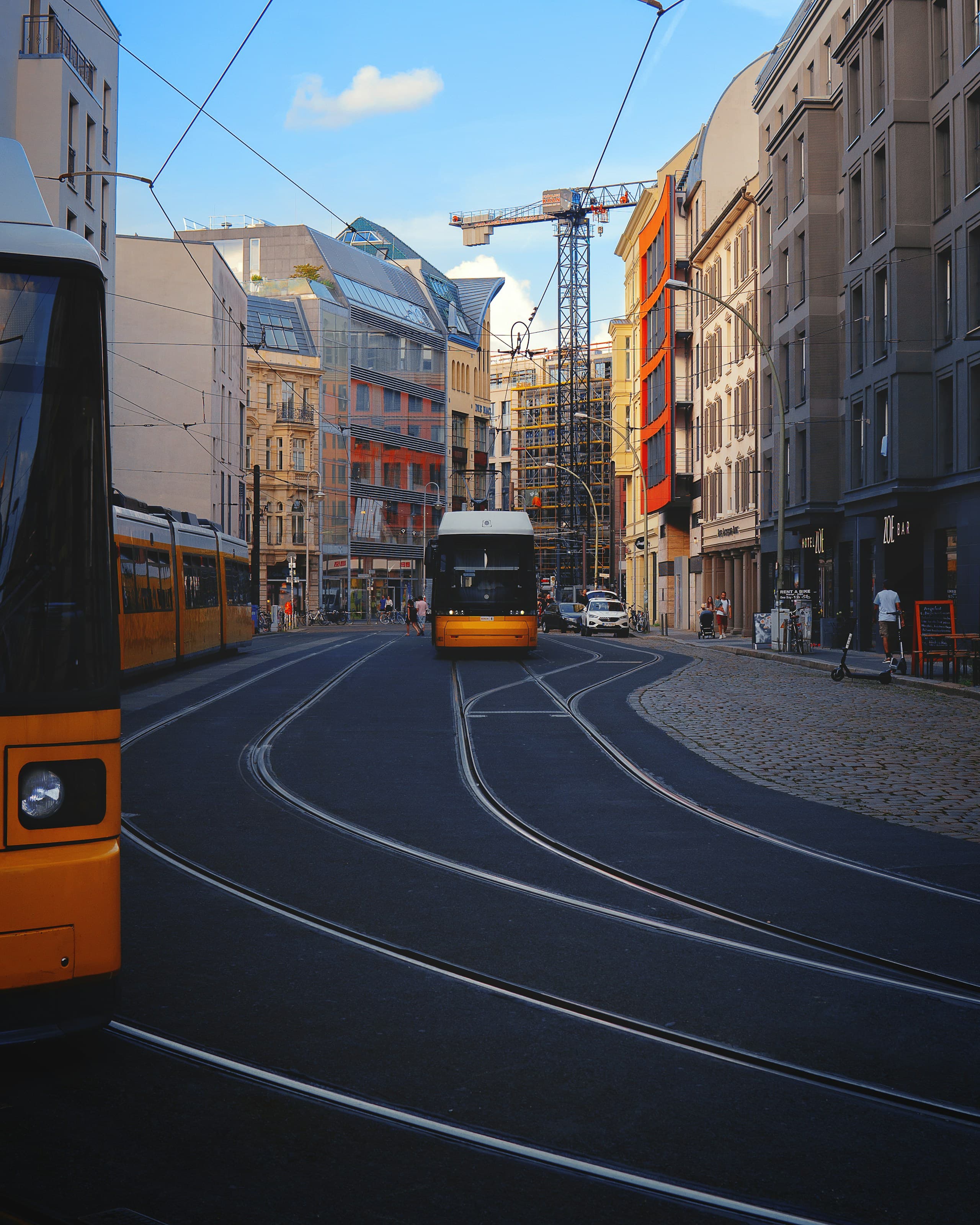 A yellow Berlin tram on a wide street in Mitte, with apartment buildings and overhead lines behind it.