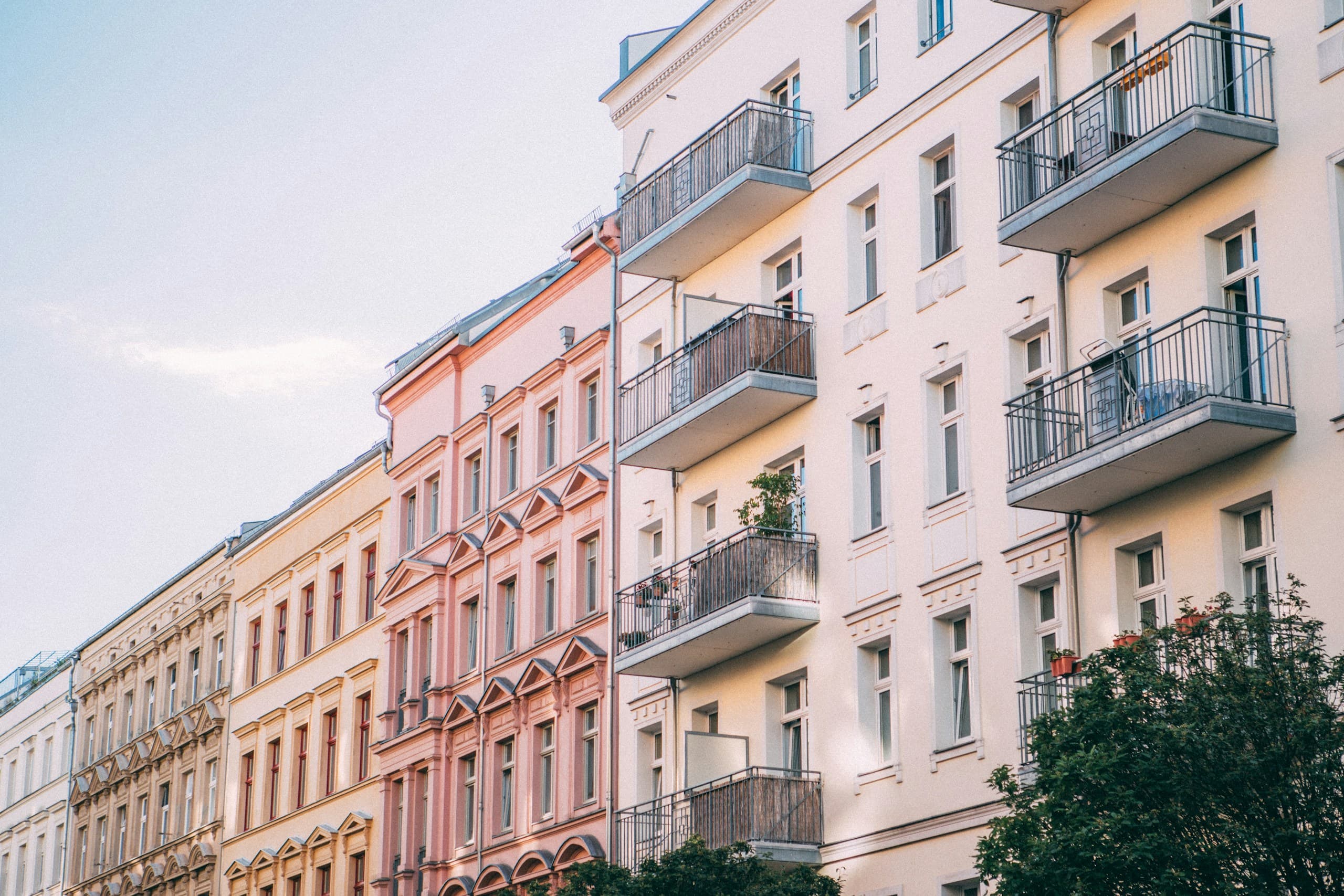 A row of pastel Altbau façades in Prenzlauer Berg seen from below, with balconies and tall windows.