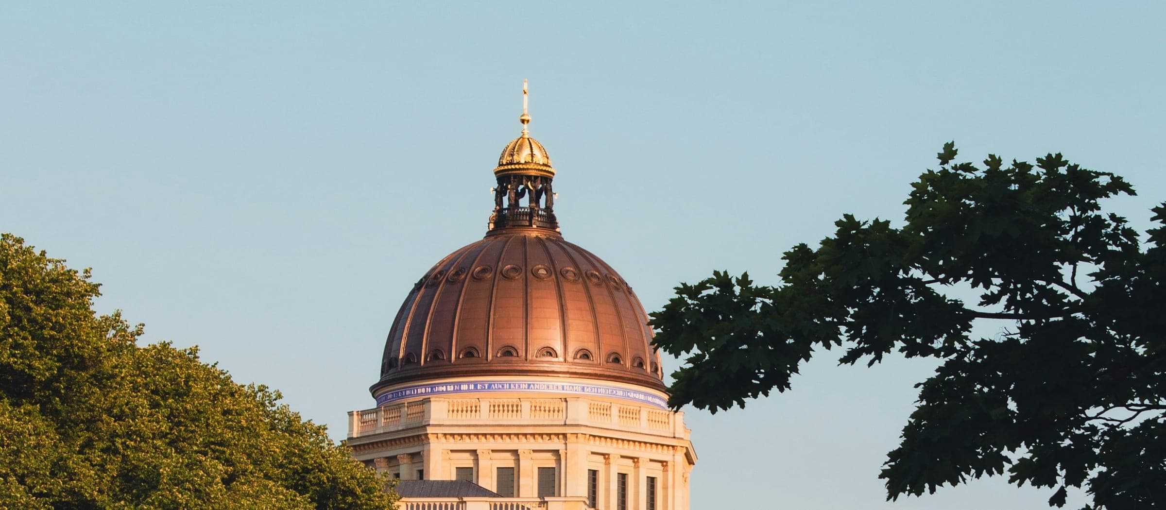 The dome of the Humboldt Forum above the trees along the Spree in Mitte, with the river in the foreground on a clear evening.