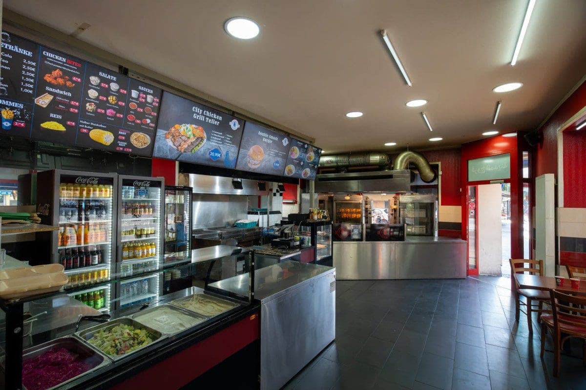 The interior seen from the doorway: illuminated menu screens along the ceiling, a drinks fridge on the left and a stainless steel counter running down the room.