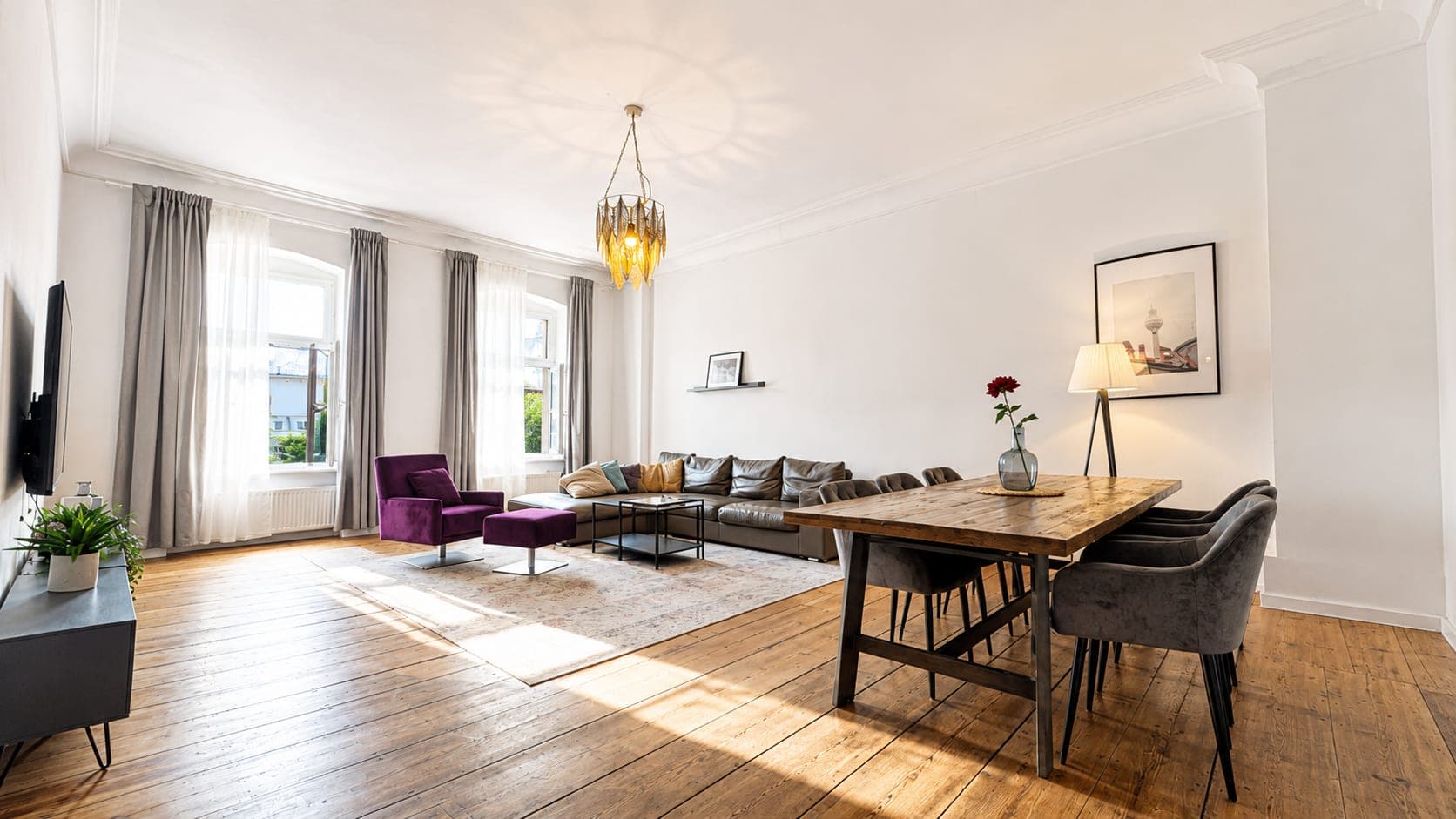 A high-ceilinged Altbau room with stucco cornices, a long wooden dining table and a brass chandelier above wide floorboards.