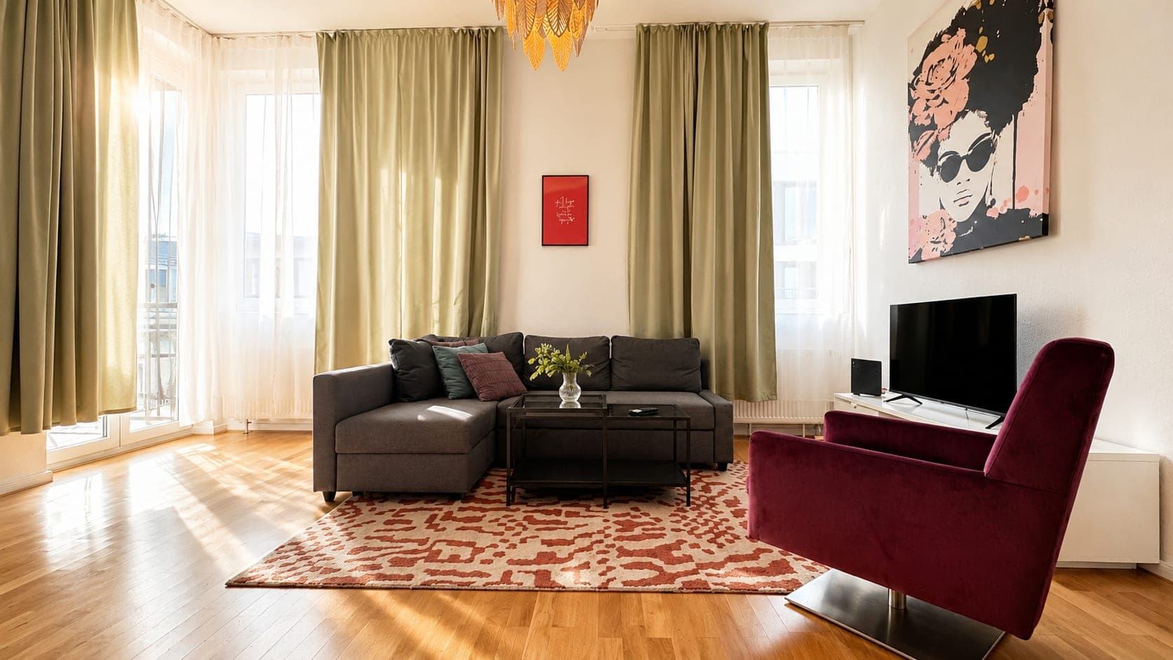 Late afternoon sun across the floorboards of a living room with olive curtains, a grey corner sofa and a burgundy armchair.